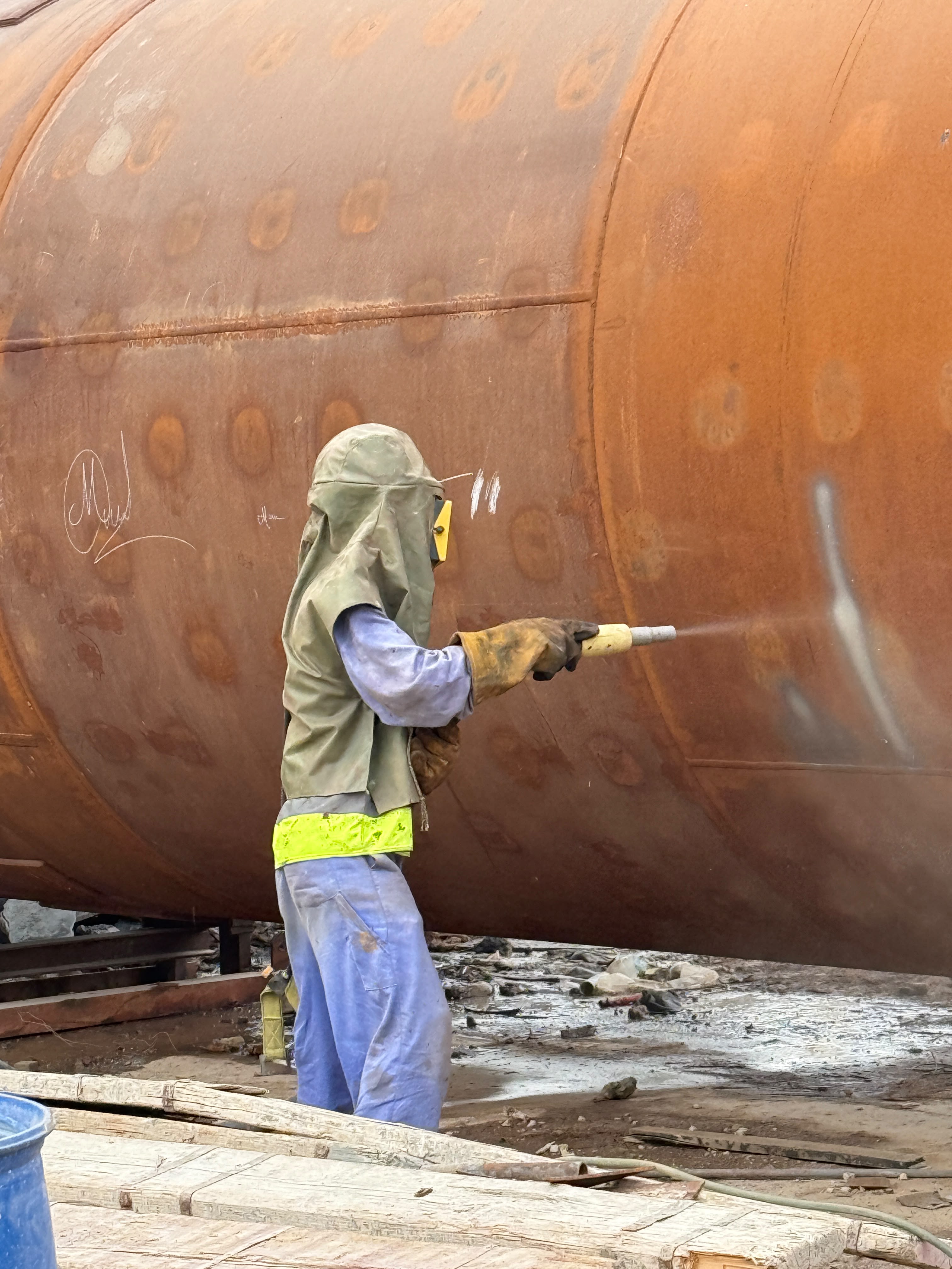 Technician in protective equipment grinding a vessel surface